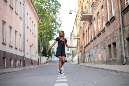 Woman walking down a street in a black dress and trainers