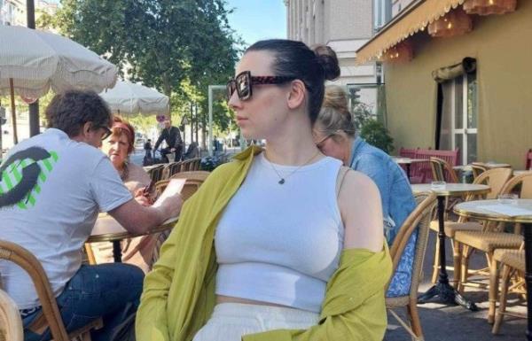 Molly sitting at a table outside a restaurant, looking to the side, with her hair in a tight bun and wearing sunglasses