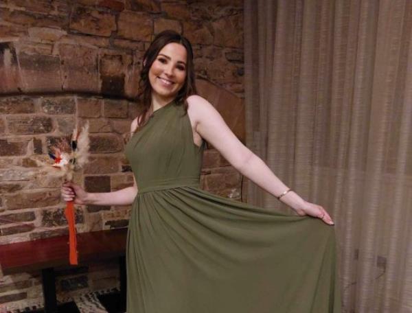 Molly in a green dress, holding flowers and smiling