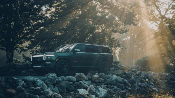 The Rivian R1S in dark green in the sunrise, front 3/4 view