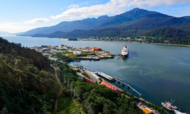 Cruise ship moored to a pier in a large sound with tree-clad mountains in the background