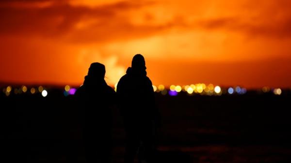 People watch as the night sky is illuminated caused by the eruption of a volcano on the Reykjanes peninsula of south-west Iceland seen from the capital city of Reykjavik, Mo<em></em>nday Dec. 18, 2023. (AP Photo/Brynjar Gunnarsson)