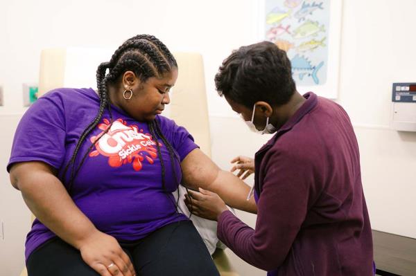 Young woman wearing purple t-shirt has long braids. Her blood is being drawn.