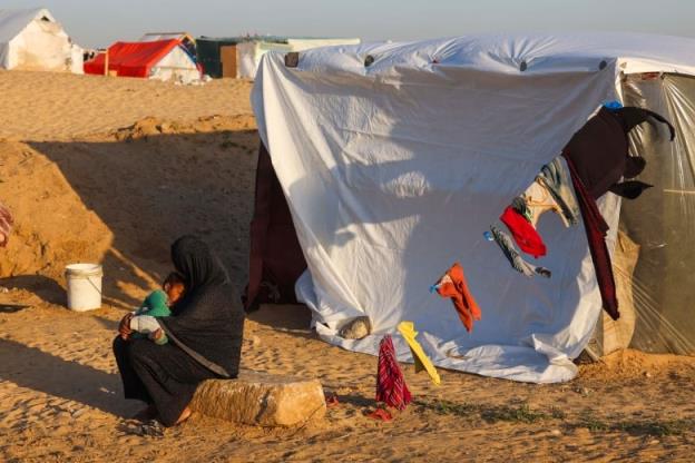 A displaced Palestinian woman cuddling her baby sits on a stone in front of her tent at a camp in Rafah on March 11, 2024, amid o<em></em>ngoing battles between Israel and the Hamas militant group. 