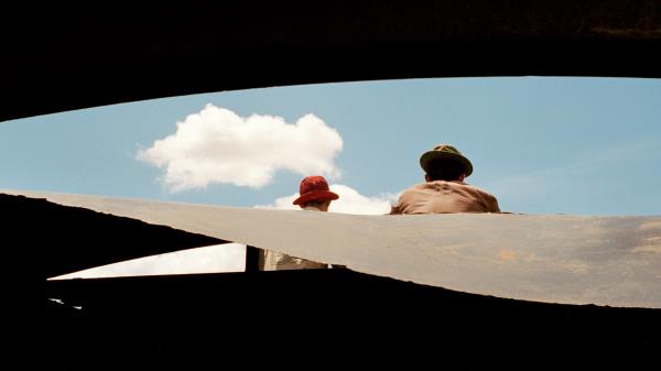 Two men wearing hats look off at a cloudy blue sky