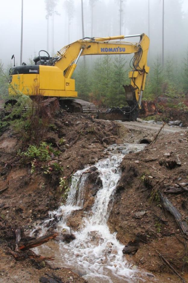 A yellow co<em></em>nstruction vehicle works near an overflowing culvert.