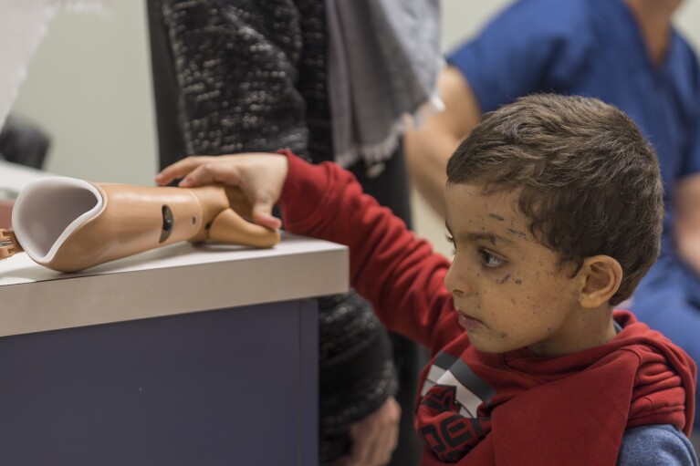 Four-year-old Omar Abu Kuwaik examines his new prosthetic arm at Shriners Children's Hospital on Wednesday, Feb. 28, 2024, in Philadelphia. Omar Abu Kuwaik is far from his home in Gaza. The 4-year-old's parents and sister were killed by an Israeli airstrike, when he lost part of his arm. (AP Photo/Peter K. Afriyie)