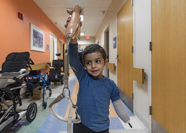 Four-year-old Omar Abu Kuwaik holds his new prosthetic arm in the air at Shriners Children's Hospital on Wednesday, Feb. 28, 2024, in Philadelphia. After his parents and sister were killed in an Israeli airstrike, Omar was pulled from the rubble and brought out of Gaza then to the United States, wher<em></em>e he received treatment, including a prosthetic arm. He spent his days in a house run by a medical charity in New York City, accompanied by his aunt. (AP Photo/Peter K. Afriyie)