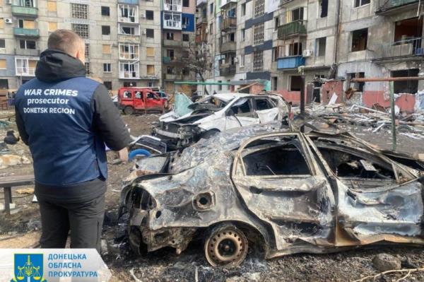 An investigator stands bear burned out cars outside an apartment building in Myrnograd