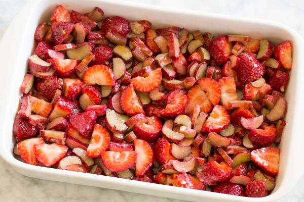 Single serving of strawberry rhubarb crisp shown in a grey bowl with ice cream on top.