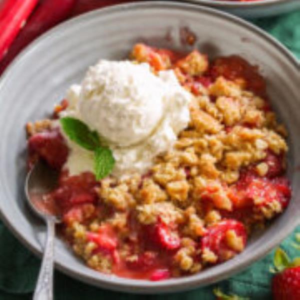 Single serving of strawberry rhubarb crisp shown in a grey bowl with ice cream on top.