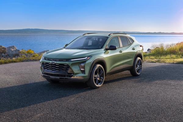 A Chevrolet Trax ACTIV in Cacti Green is parked on a road in front of a lake. Pre-production model shown. Actual production model may vary. Available in spring 2023. Cacti Green exterior color late availability.