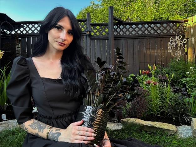 Woman sitting in black dress holding a plant in a garden.