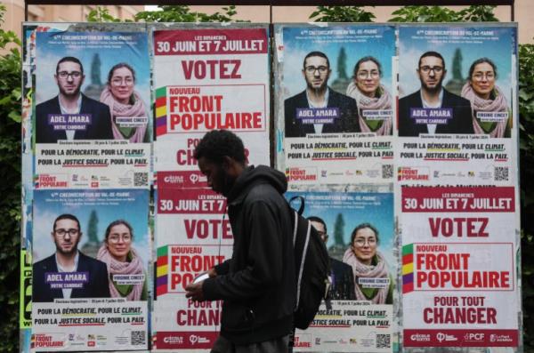 A man walks past election posters of the Nouveau Front Populaire