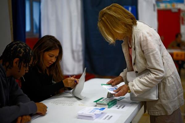 A voter takes ballots from a stack displayed on tables in the second round of the early French parliamentary elections, at a polling station in Paris, France, July 7, 2024. REUTERS/Sarah Meyssonnier