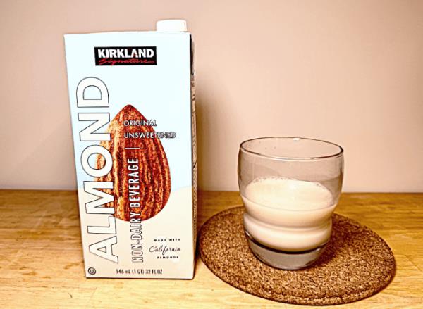 a co<em></em>ntainer of three trees almond milk next to a glass of it 