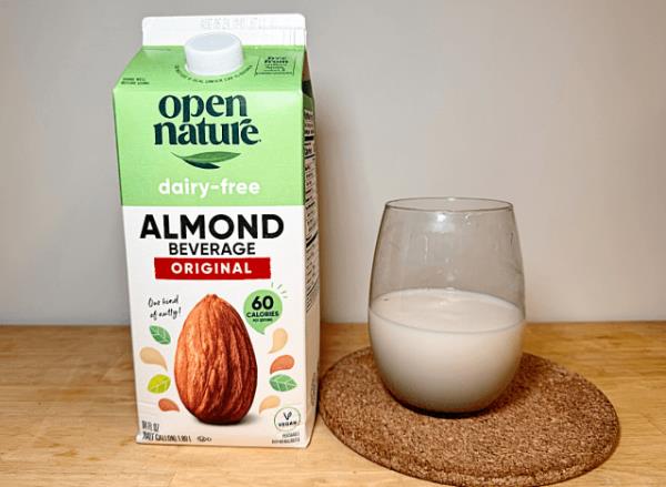 a co<em></em>ntainer of open nature almond milk next to a glass of it 