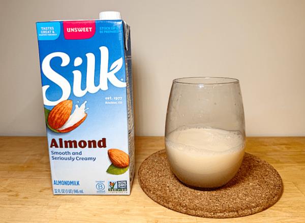 a co<em></em>ntainer of silk almond milk next to a glass of it 