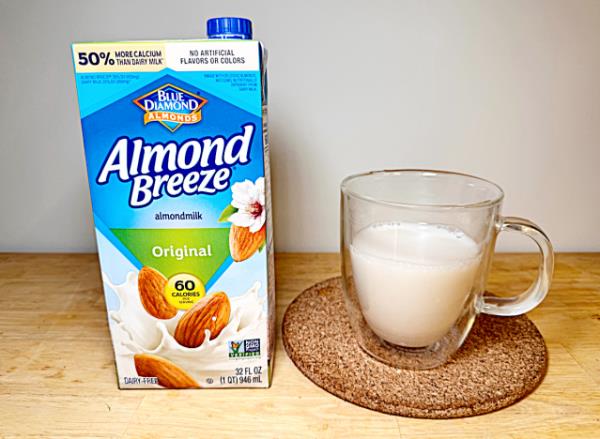 a co<em></em>ntainer of almond breeze almond milk next to a glass of it 