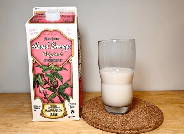 co<em></em>ntainer of trader joe's almond beverage next to a glass of it 