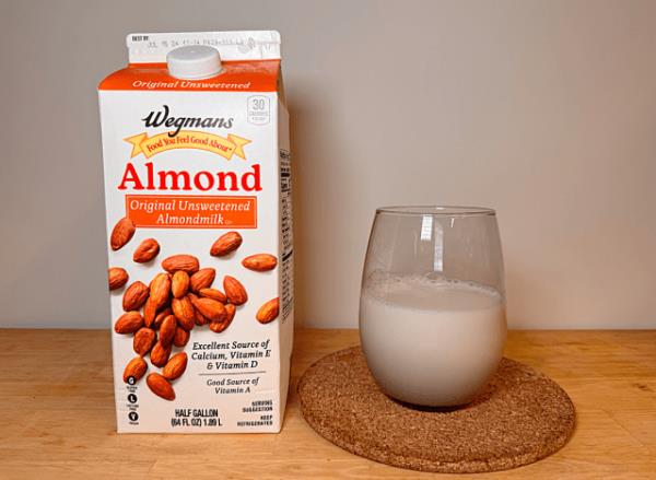 a co<em></em>ntainer of wegman's almond milk next to a glass of it 