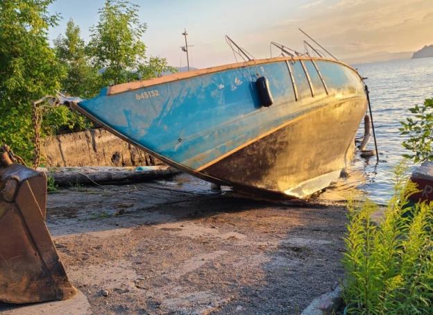 An old, battered sailboat on the shore among some pieces of rusty me<em></em>tal.