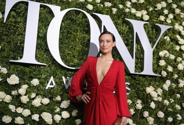 Olivia Wilde on the Tony Awards red carpet,in red gown against a green grass backdrop. 