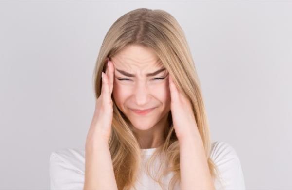 Young woman with a headache holds her temples with her hands.