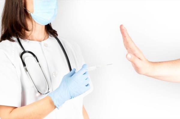 Doctor with a syringe of COVID-19 vaccine and a patient's hand refusing.