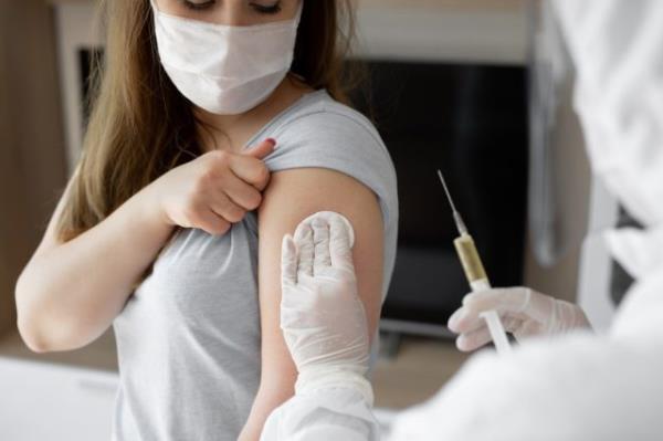 Doctor in perso<em></em>nal protective suit or PPE inject vaccine shot to stimulating immunity of woman patient at risk of coro<em></em>navirus infection.