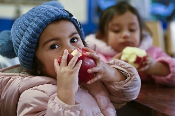 Two young girls eat apples.