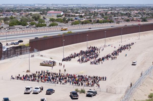 Migrants who crossed the U.S.-Mexico border wait by the U.S. border wall for U.S. Customs and Border Protection officers to admit them into the United States for processing on Thursday, May 11, 2023 in El Paso, Texas.  