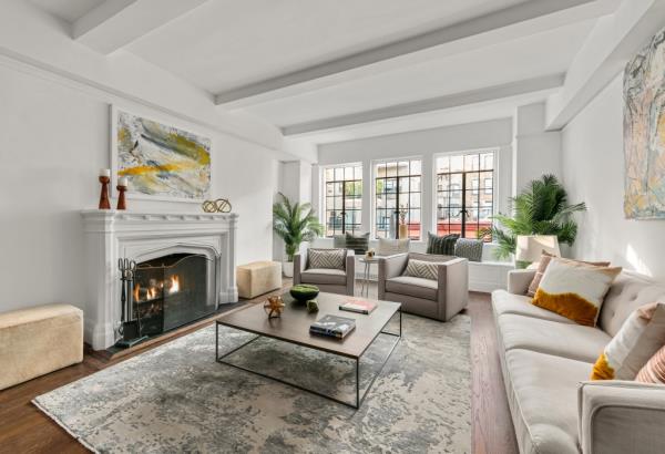 The Village home sports beamed ceilings and a living room with a woodburning fireplace and an original stone mantel, as seen in this image showing the unit in its most current state.