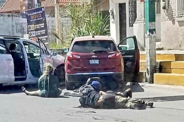 A woman sits on the roadbed and three men lay on the street behind cars crashed together