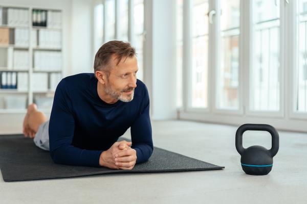 Man resting on a gym mat alo<em></em>ngside a kettle weight as he takes a break from working out in a health and fitness concept