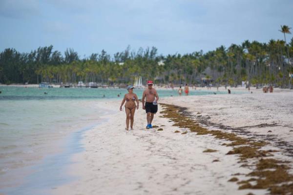 Tourists walk along the shore of the beach partially covered by sargassum at Bibijagua Beach in Punta Cana, Dominican Republic.