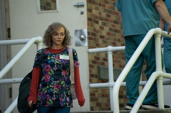 Christina Ricci in a curly wig and glasses walking outside. 