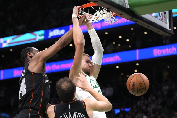 Boston Celtics center Kristaps Porzingis, right, slams a dunk against Detroit Pistons guard Alec Burks, left, and Detroit Pistons forward Bojan Bogdanovic during overtime of an NBA basketball game, Thursday, Dec. 28, 2023, in Boston. The Celtics defeated the Pistons 128-122. (AP Photo/Charles Krupa)