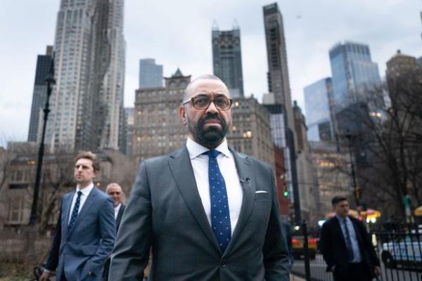 Home Secretary James Cleverly walking along a street in a suit flanked by two other men in suits