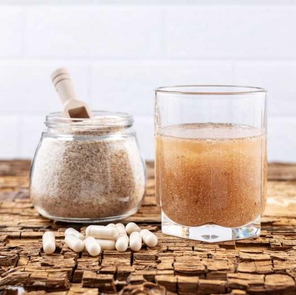 psyllium capsules and a glass of water and psyllium husk on an old wooden board