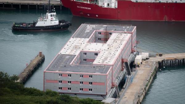 A tug boat passes the Bibby Stockholm accommodation barge at Portland Port in Dorset, which will house up to 500 people. The Home Office have said around 50 asylum seekers would board the Bibby Stockholm, with the numbers rising to its maximum capacity over the coming months, despite safety co<em></em>ncerns raised by some of the county's Co<em></em>nservative MPs and locals. Picture date: Thursday August 3, 2023.