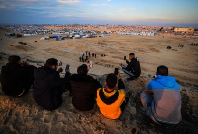 Displaced Palestinians on a hill attempt to get a signal in order to co<em></em>ntact their relatives.