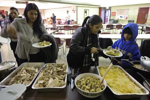 Angeliana Montaner, left, and Maria Goitia put turkey and side dishes on their plates during a potluck Thanksgiving dinner at St. Agatha Catholic Church in Chicago on Nov. 21, 2023.