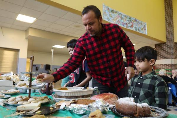 Pablo Lopez reaches for traditio<em></em>nal Venezuelan coo<em></em>kies called polvorosas to give to his son Paul, 6, during a potluck Thanksgiving dinner with students, teachers and parents at Chappell Elementary School in Chicago on Nov. 22, 2023. 