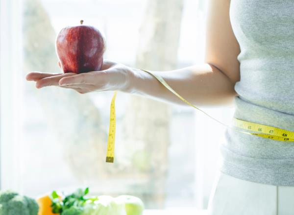 woman holding apple and tape measure, co<em></em>ncept of how to lose one pound a week without exercise