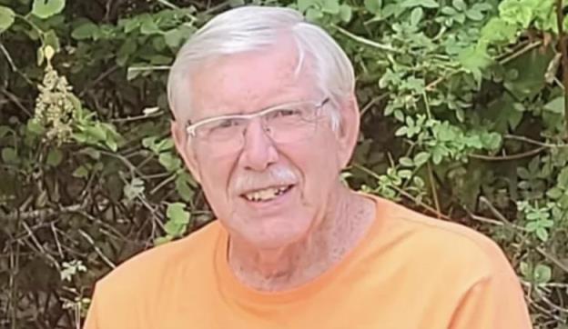 A man poses in front of a bush.