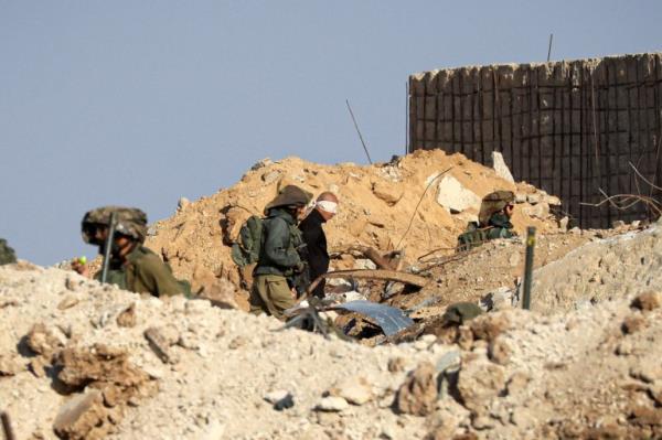 Israeli soldiers detain blindfolded Palestinian men in a military truck while watching Palestinians (not pictured) fleeing the fighting in war-torn Gaza walk by on a road in the Zeitoun district of the southern part of the Gaza Strip on November 19, 2023.