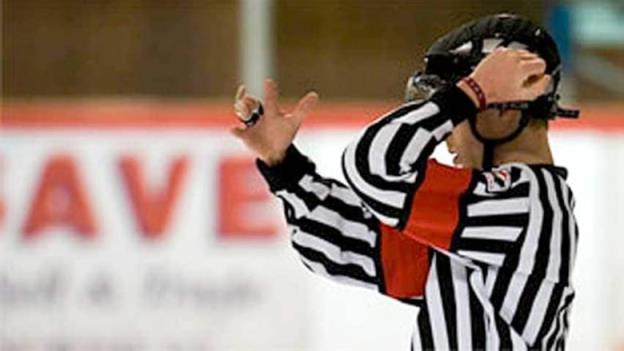 A young hockey referee wears a black-and-white striped uniform and helmet. 