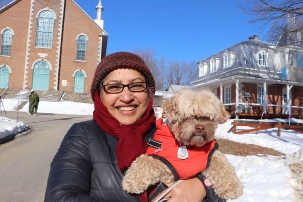 A woman smiles at the camera holding her dog. She is standing in front of a church.