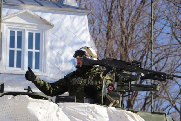 A man in military uniform gives a thumbs up. He is on a light armoured vehicle. 